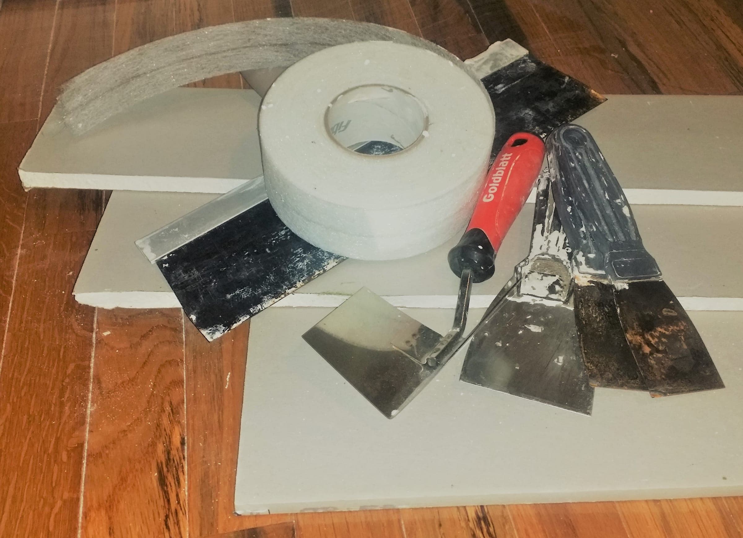 Drywall tape, taping knives and a mud pan resting on a sheet of drywall