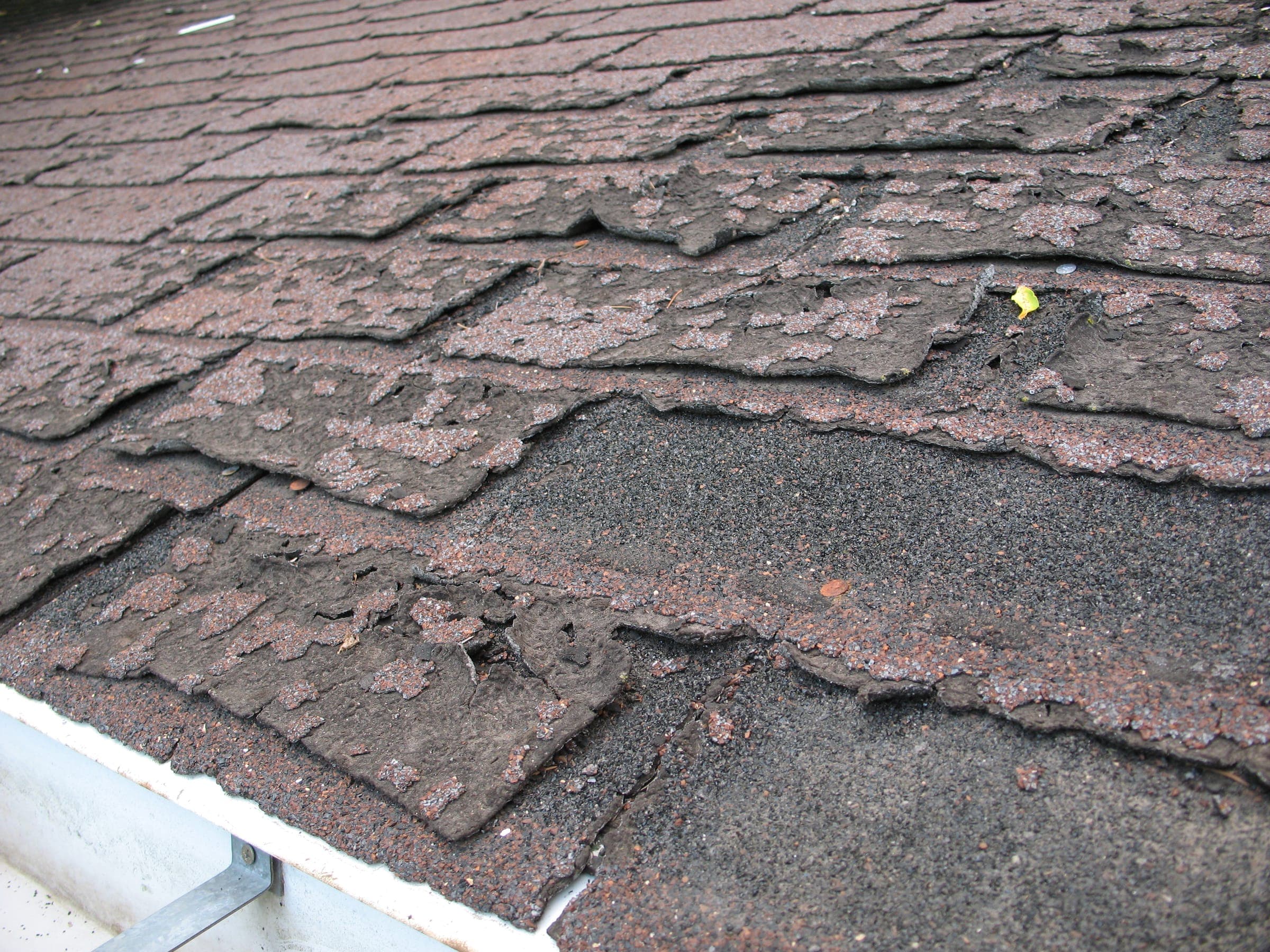 Worn, cracked asphalt shingles that are letting water into a roof
